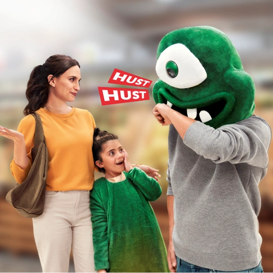 Mutter, Vater und Tochter stehen beieinander. Die Tochter trägt das Kostüm eines Hustenmonsters. Der Vater hat den Kopf des Kostüms auf.